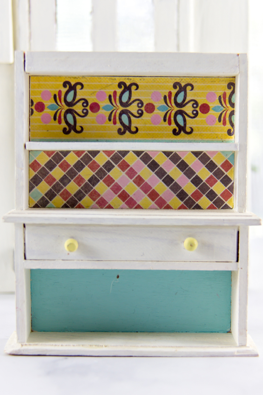 a bookshelf and drawer for a dollhouse finished with scrapbook paper and paint