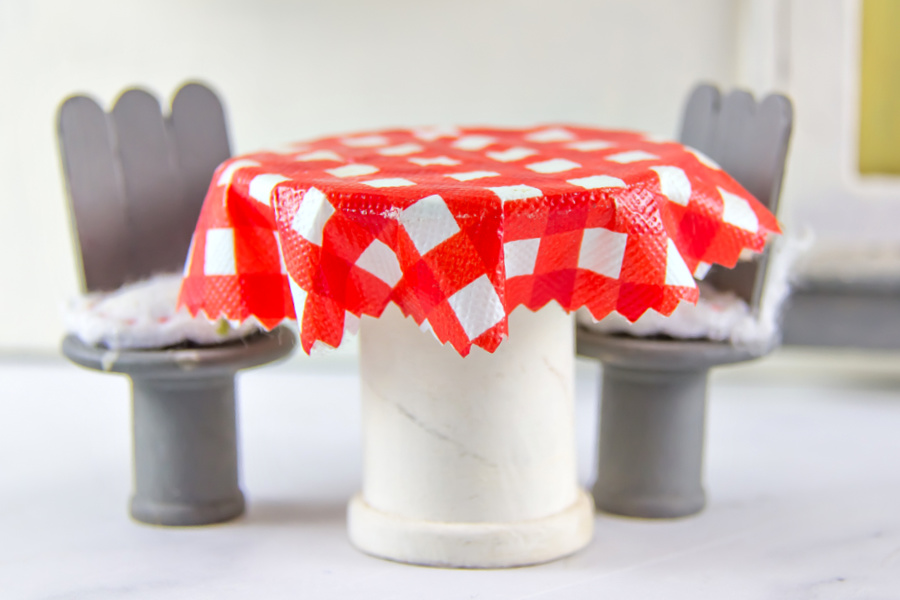 A handmade table and chairs for a dollhouse using popsicle sticks and wood spools.