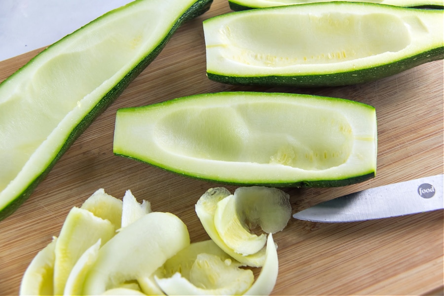 A zucchini being hollowed out using a melon baller to make stuffed zucchini boats.