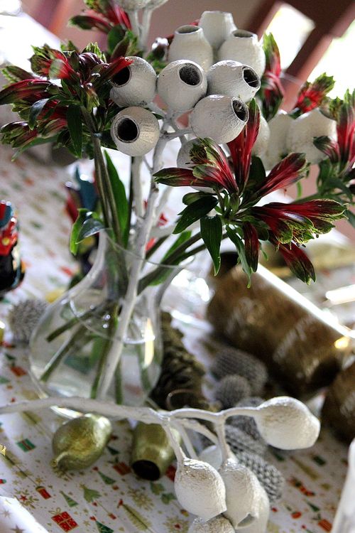 New Zealand Christmas Bell flowers in a vase surrounded by painted gumnuts on a Christmas table. 