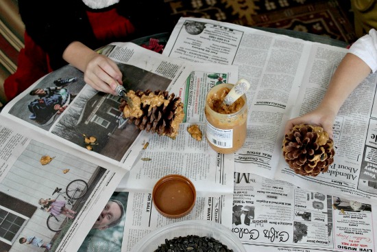 kids spreading peanut butter on pinecones to make bird feeders