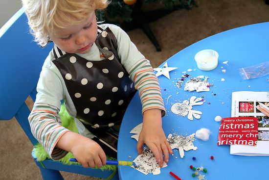 a boy decorating paper christmas ornaments with glitter