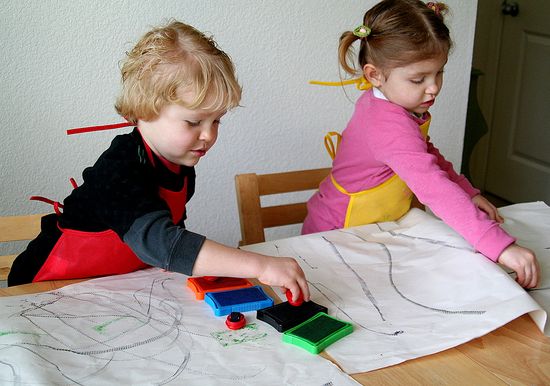 Kids making tire track wrapping paper by rolling cars and tires over a stamp pad and onto paper.