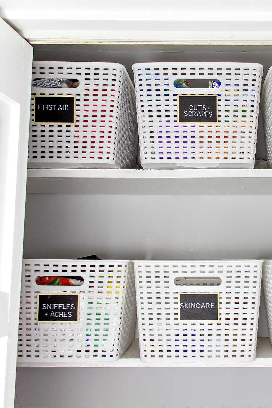 White bathroom closet with shelves and white baskets with chalkboard organization labels.