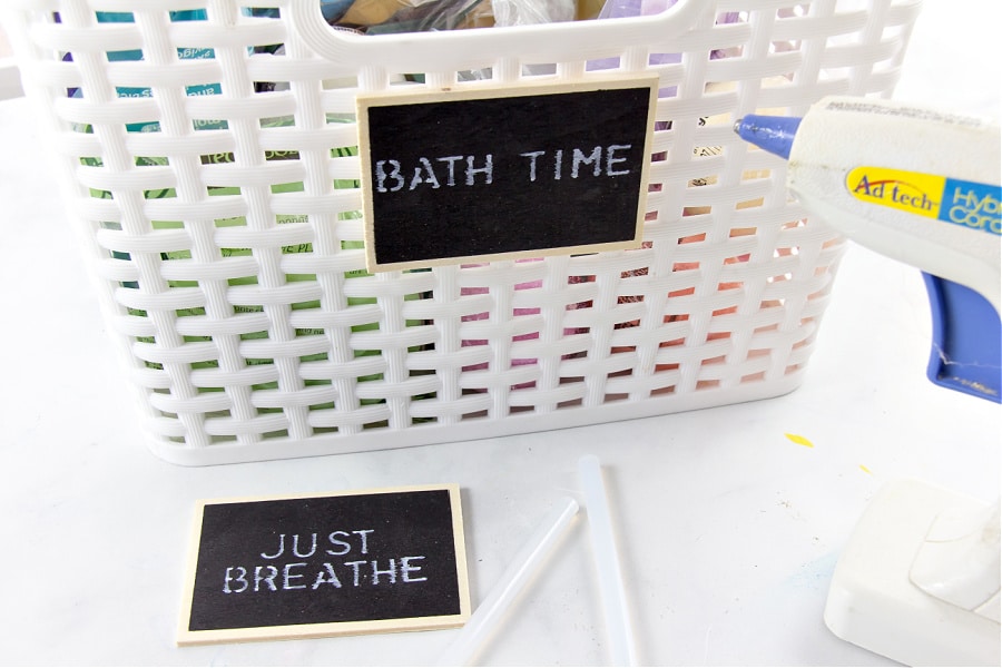 Hot glue being used to attach chalkboard bathroom organization labels to storage baskets.