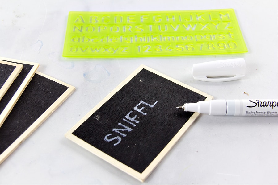A Sharpie and a letter stencil being used to make chalkboard bathroom organization labels.