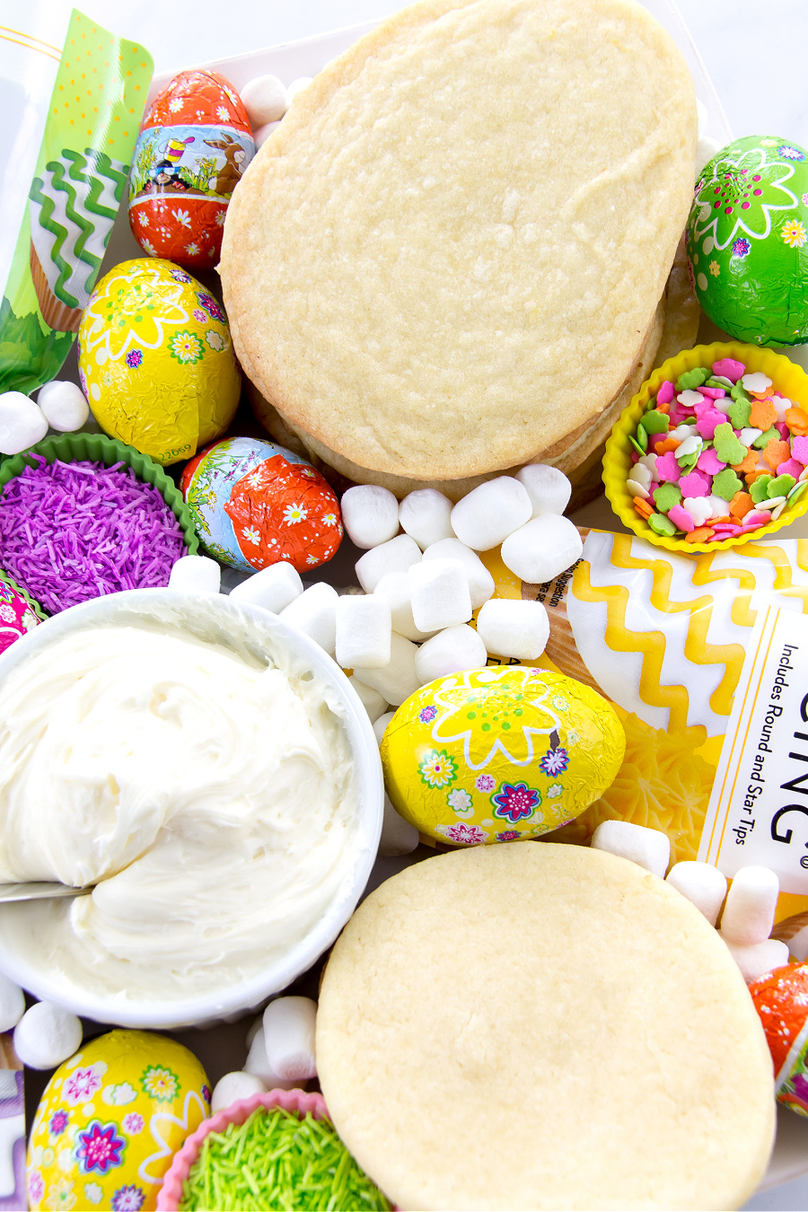 Egg-shaped sugar cookies, toppings, and icing on a food tray for kids to decorate cookies at an Easter party.