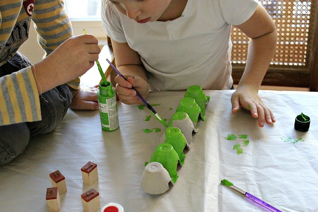 kids painting an egg carton with green paint to make a caterpillar craft