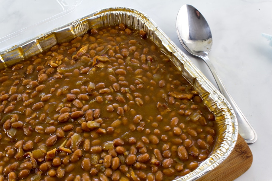 a foil baking dish filled with baked beans and bacon for a potluck. 