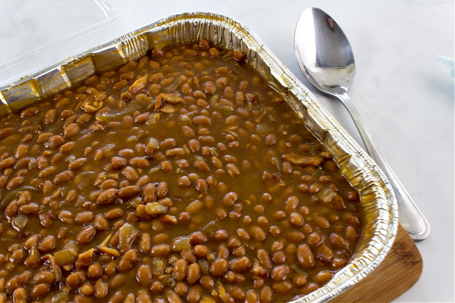 a foil baking dish filled with baked beans and bacon for a potluck. 