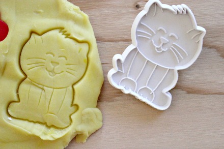 A cat cookie cutter being used on homemade yellow playdough.