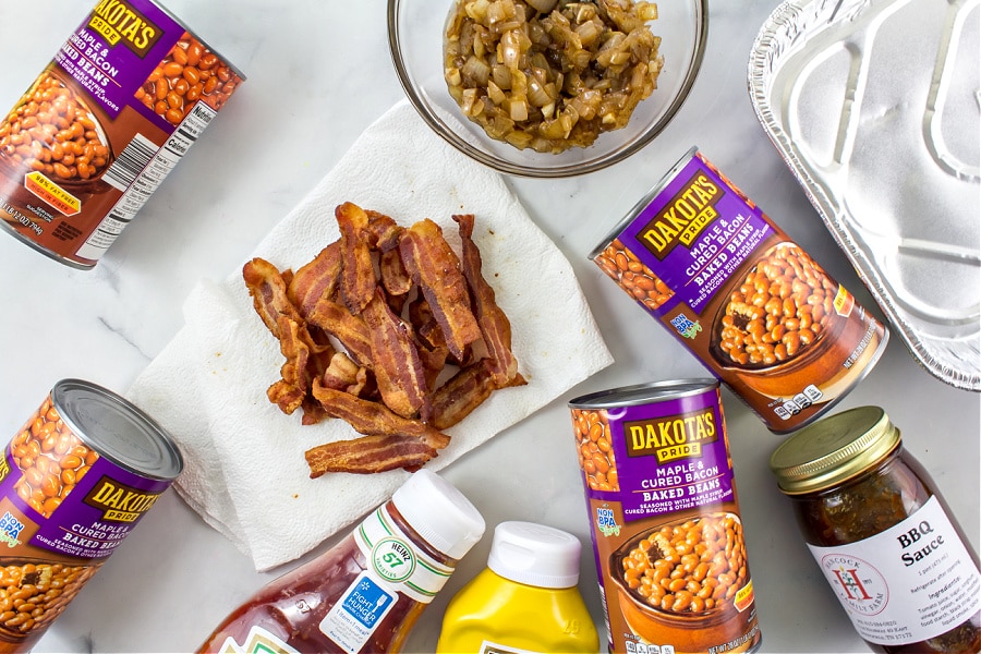 To make baked beans with bacon in the oven you will need cans of maple bacon baked beans, cooked bacon, onion, and BBQ sauce. 