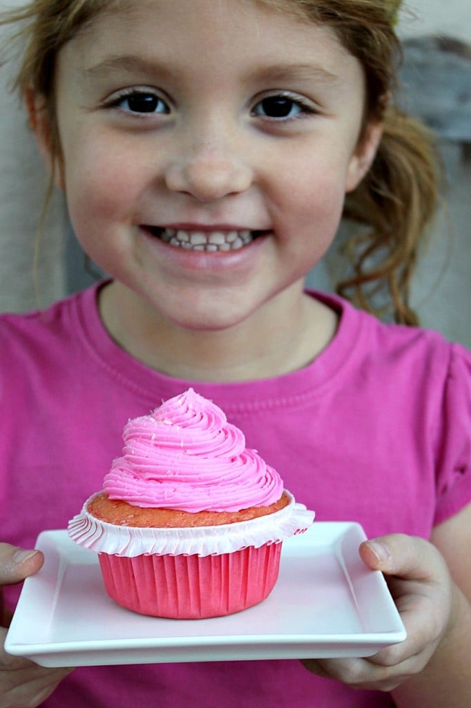 A little girl holding a pink cupcake topped with pink frosting for a Pinkalicious treat.
