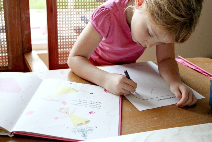 A girl reading the Pinkalicious book and drawing a picture.