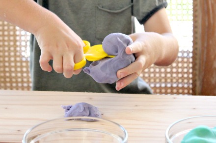 A boy cutting homemade purple playdough with playdough scissors.