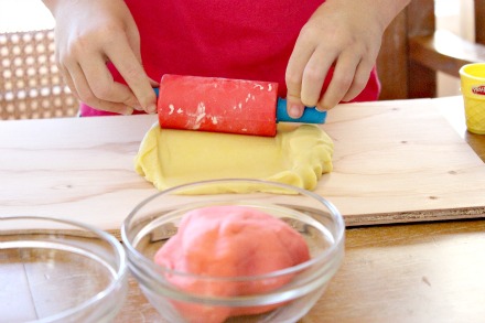 Homemade yellow playdough being rolled out with a playdough rolling pin.