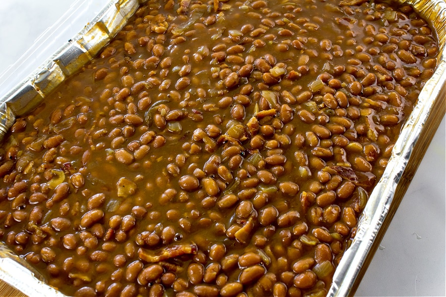 a foil tray filled with baked beans and bacon for a potluck.