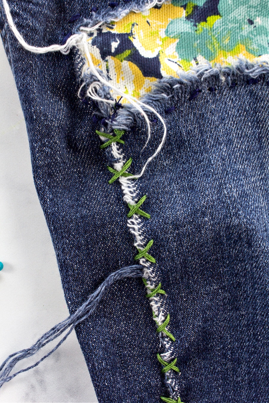 A tear in denim jeans being repaired by sewing crosses using embroidery thread.
