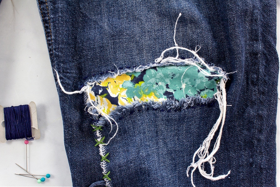 Step 2 for repairing ripped denim jeans is to sew a canvas patch inside the hole using embroidery thread.