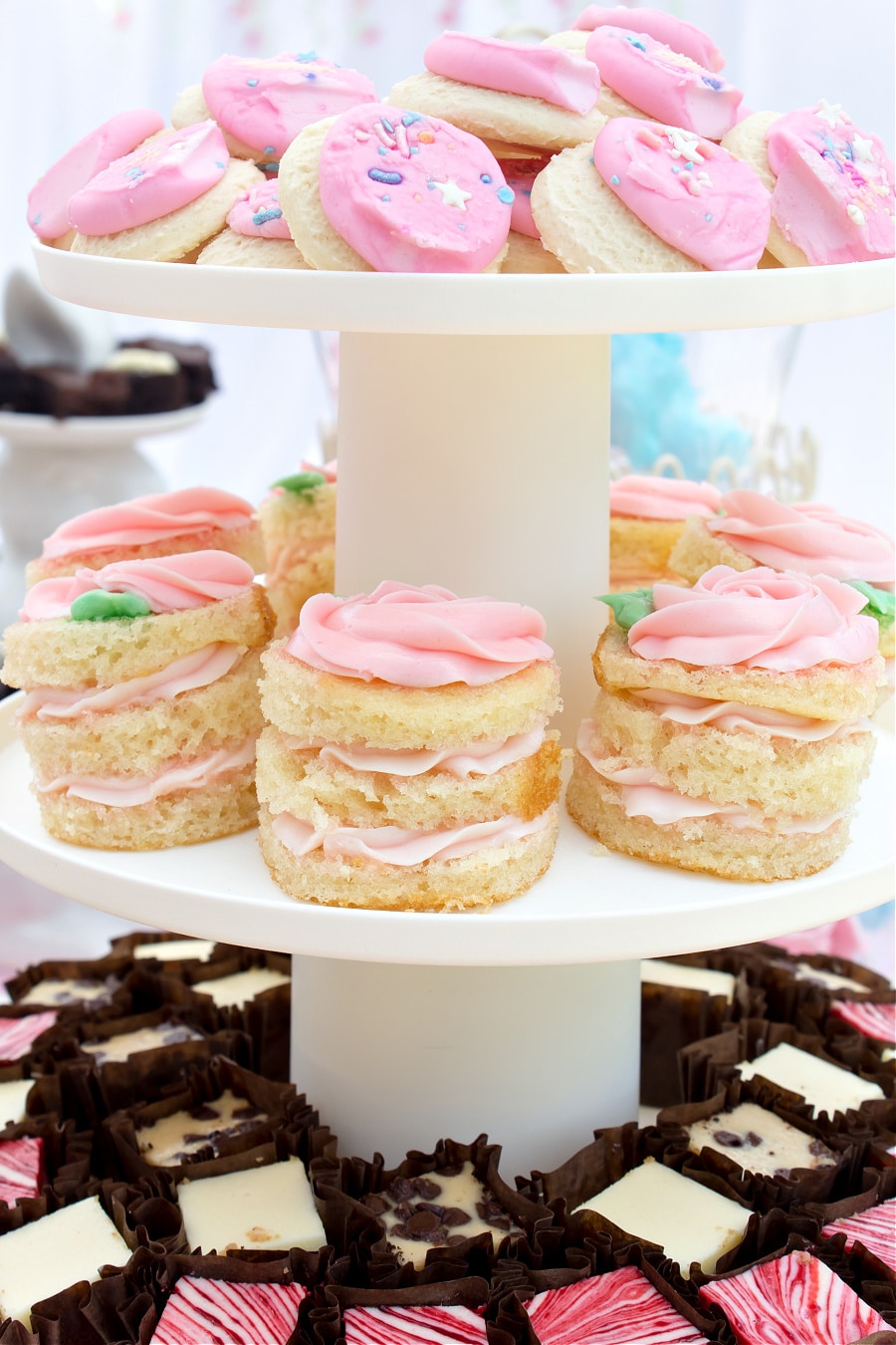 A tiered dessert tray with mini stacked cakes, frosted cookies, and cheesecake bites for a tea party.