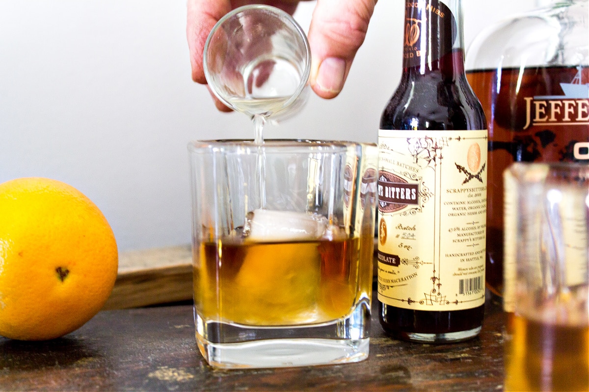 orange simple syrup being added to an old fashioned drink