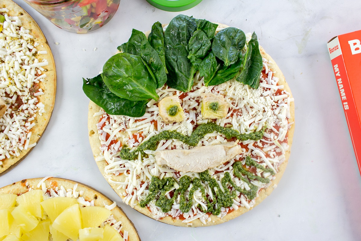 A funny face pizza decorated using chicken, pesto, and spinach.