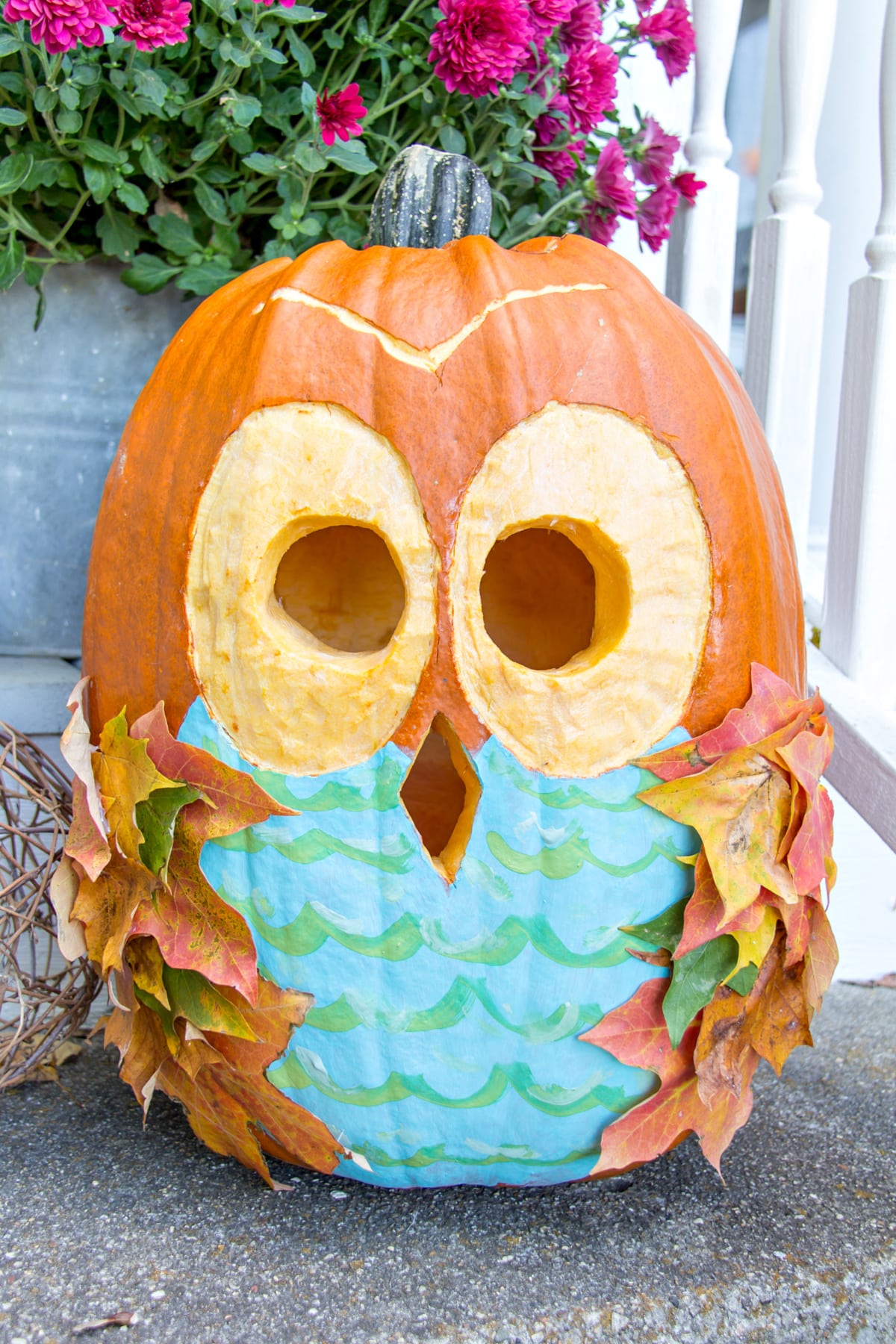 a pumpkin carved and painted to look like an owl with fall leaves used as feathers