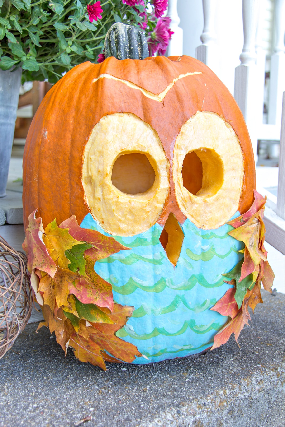 An owl pumpkin that has been painted and carved. Fall leaves have been attached for the wings.