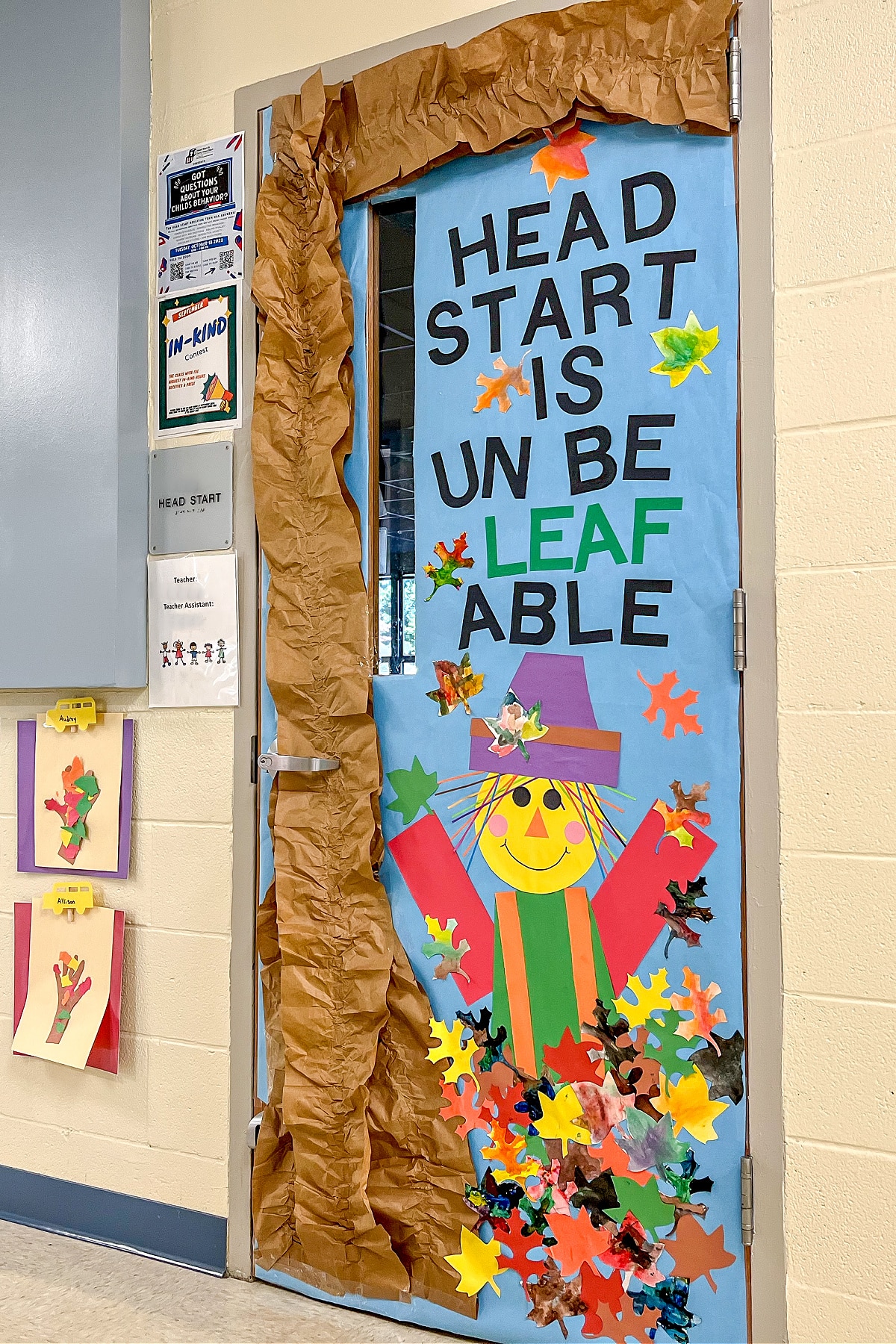 A preschool classroom door with watercolor fall leaves and a construction paper scarecrow.