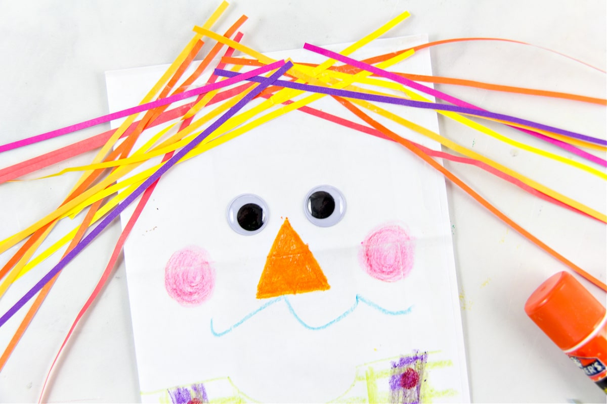 an adorable and colorful scarecrow made out of a paper bag and colorful strips of paper