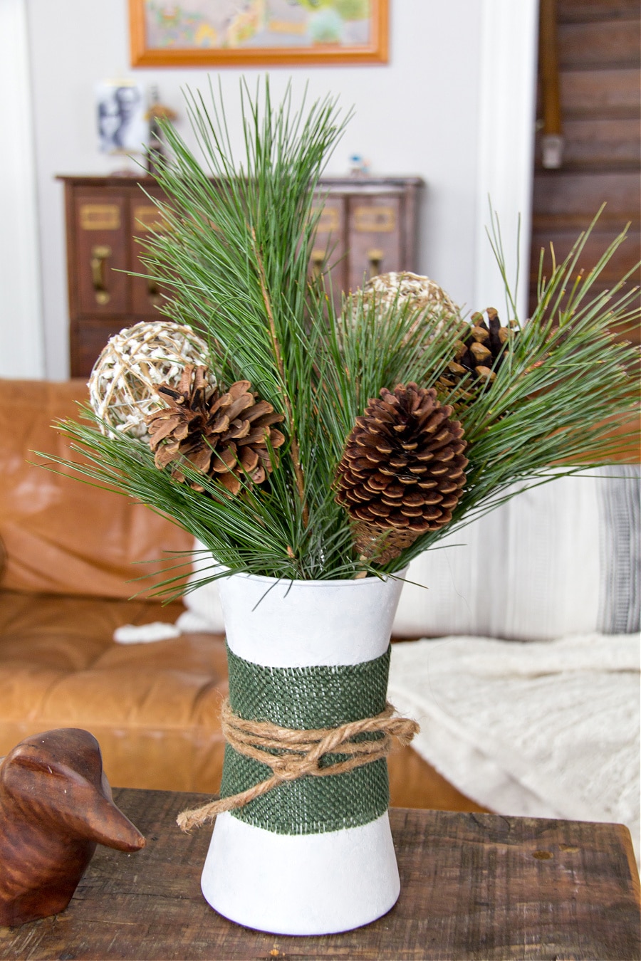 a plain glass vase painted white and wrapped with burlap and twine and filled with a winter arrangement