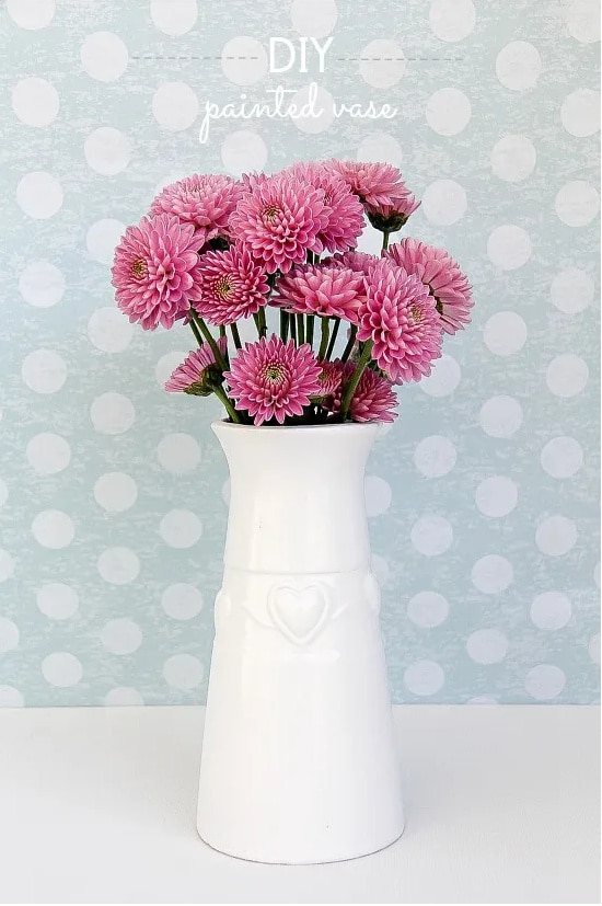A vase that has been painted white and has pink flowers inside it