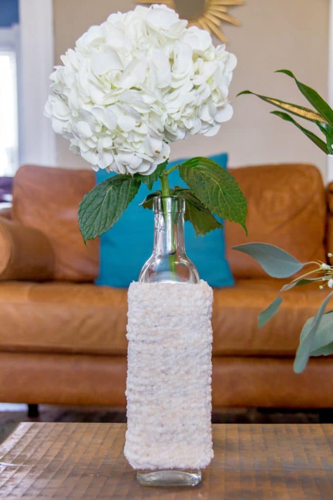 a knit winter vase cover on a glass bottle with a flower