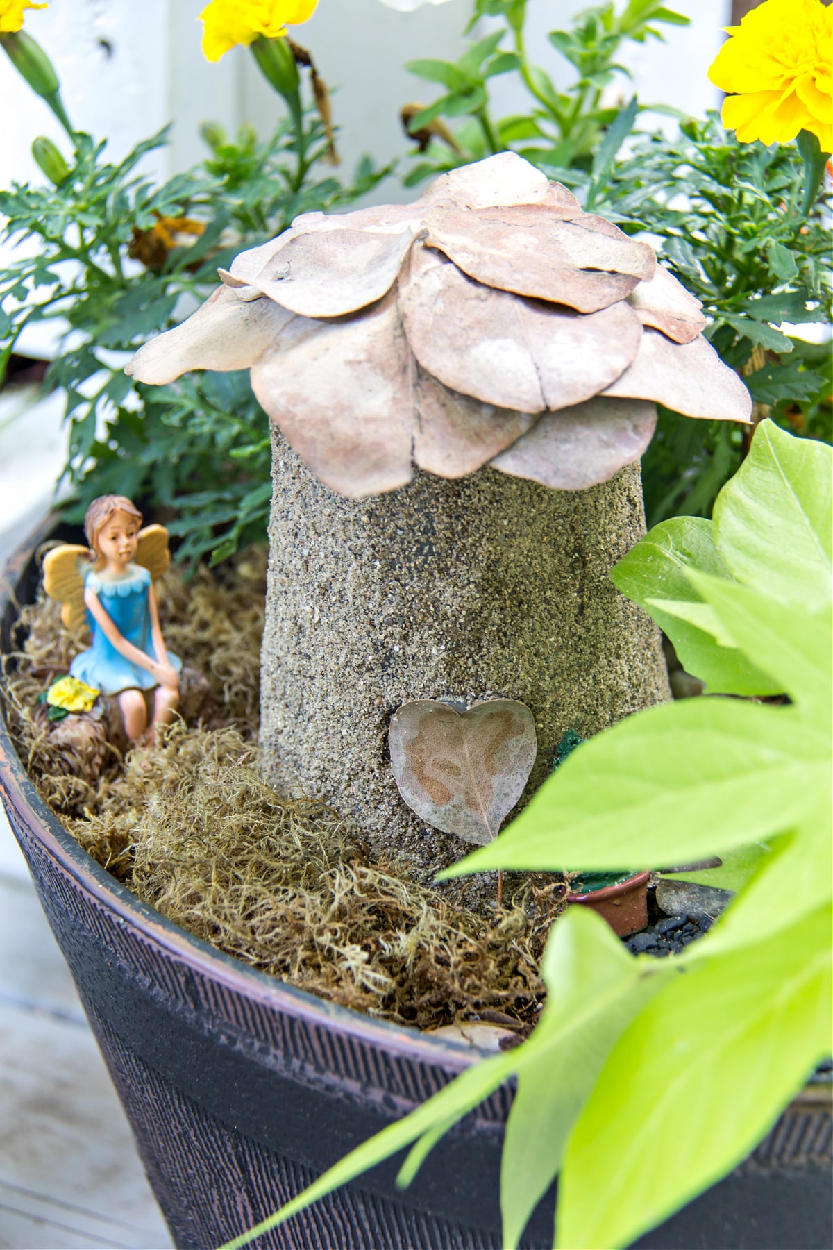 a diy fairy house made out of a plastic cup, sand, and dried leaves.