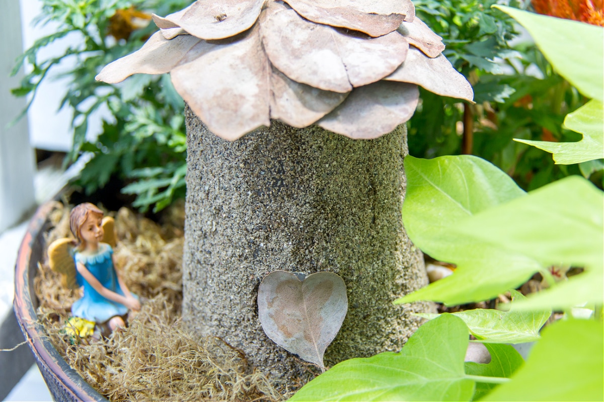 a fairy house made out of a plastic cup, cardboard, leaves, and sand. 
