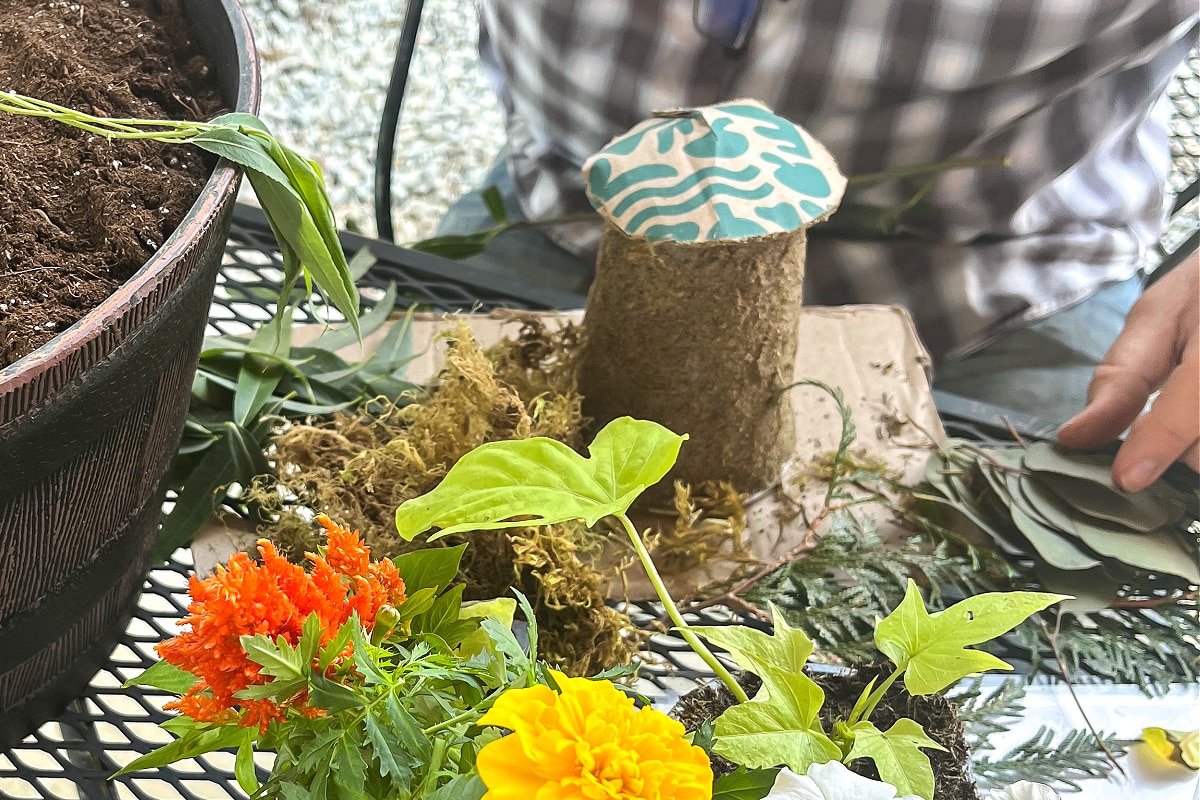 a fairy house made out of a plastic cup, leaves, sand, and cardboard.