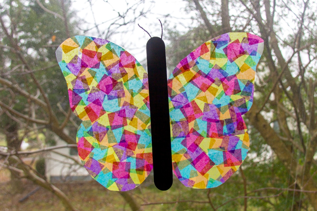 a butterfly suncatcher craft made out of tissue paper squares and contact paper