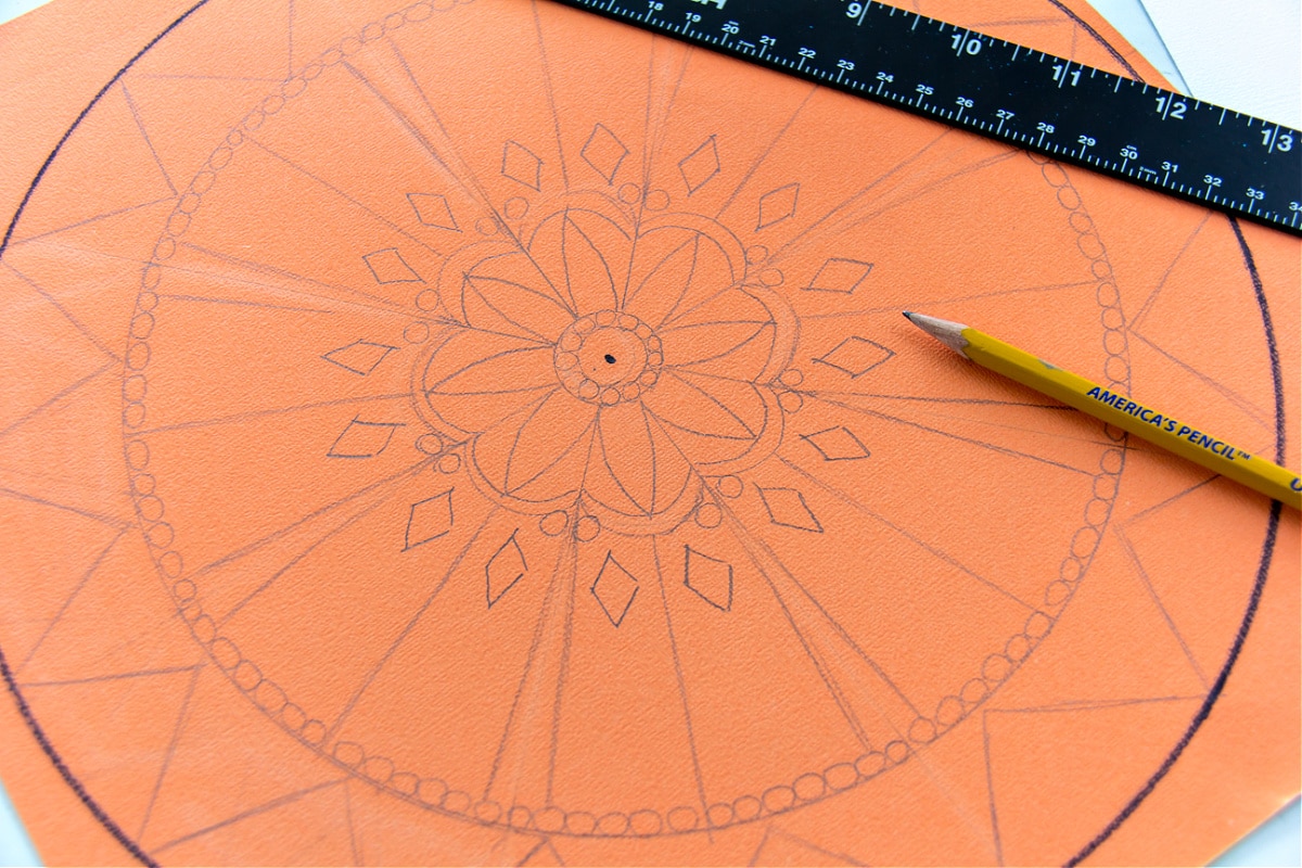 a mandala sun being drawn on orange paper