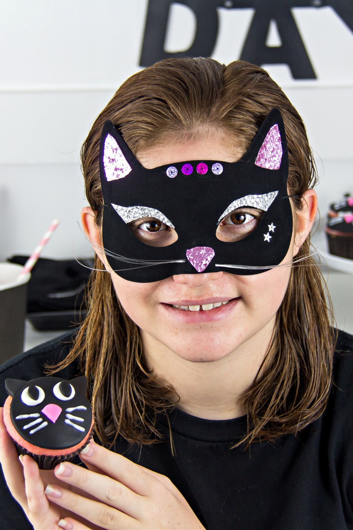 a girl wearing a black cat mask and holding a black cat cupcake for a black cat day party