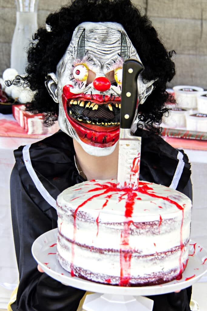 Slasher teen halloween party with a slasher costume and a cake dripping in blood with a knife in it.