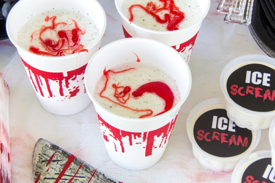 vanilla milkshakes in a cup with blood dripping down the sides and topped with strawberry topping.